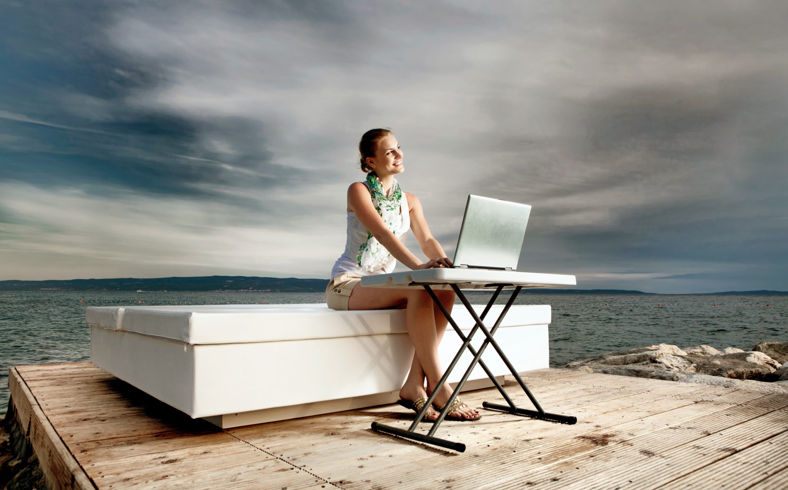 woman in white tank top sitting on white chair using macbook
