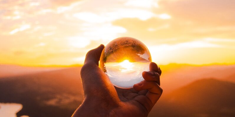 person holding glass ball reflecting sun