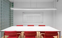Interior of office with white table near red stools and whiteboard on wall near lamp and glass wall