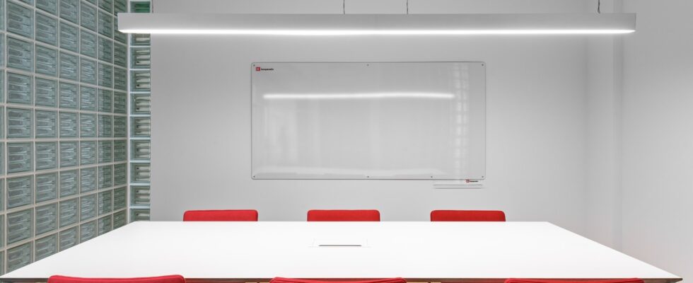 Interior of office with white table near red stools and whiteboard on wall near lamp and glass wall