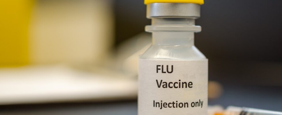 A vial of flu vaccine with a syringe at the background