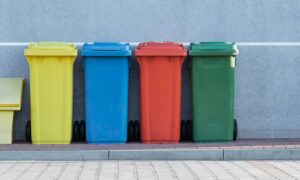 four assorted-color trash bins beside gray wall